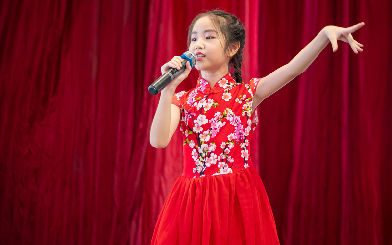 A girl singing in front of a red curtain.